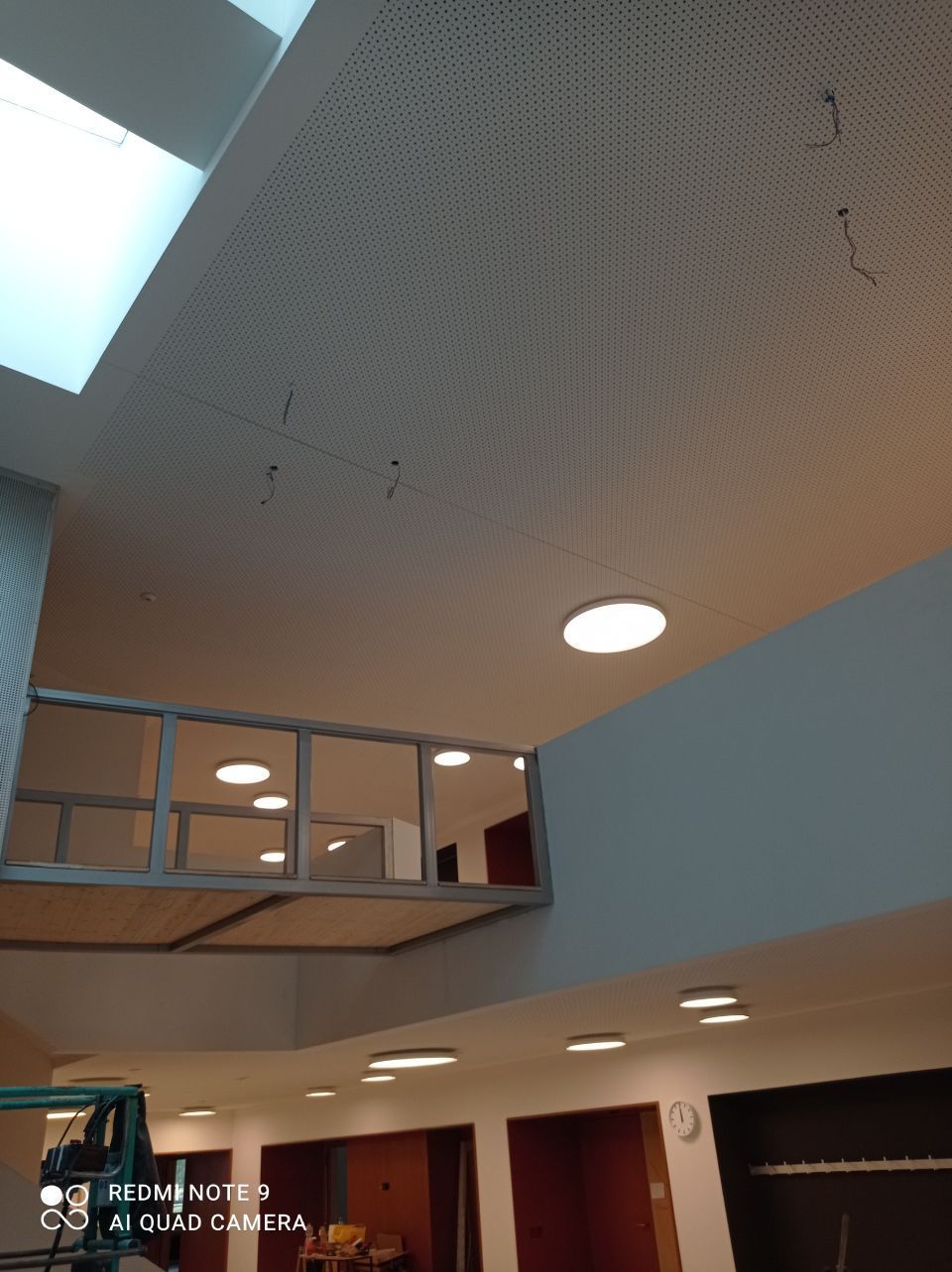 Eine Ansicht aus der Froschperspektive auf das Innere eines modernen Gebäudes mit perforierter Decke & einem verglasten Loft.