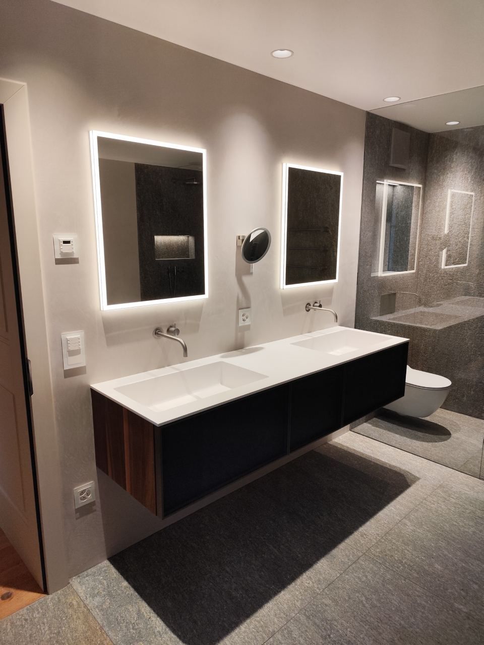 Modernes Badezimmer mit Waschtisch, beleuchteten rechteckigen Spiegeln, einem schwebenden Schrank und einer weissen Toilette.