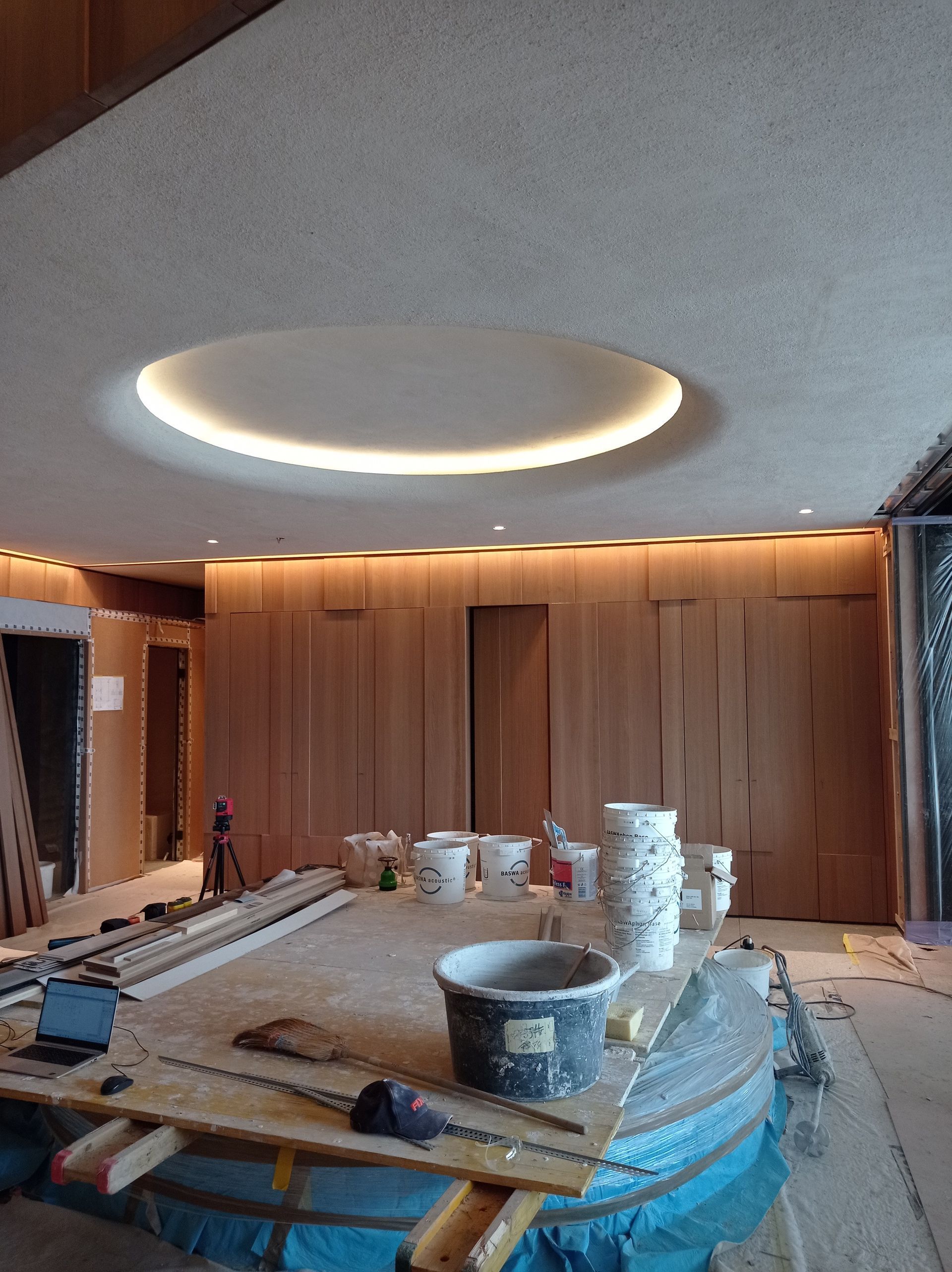 Wohnzimmer im Umbau mit Deckenleuchten, holzgetäfelter Wand und abgedeckten Möbeln und Werkzeugen