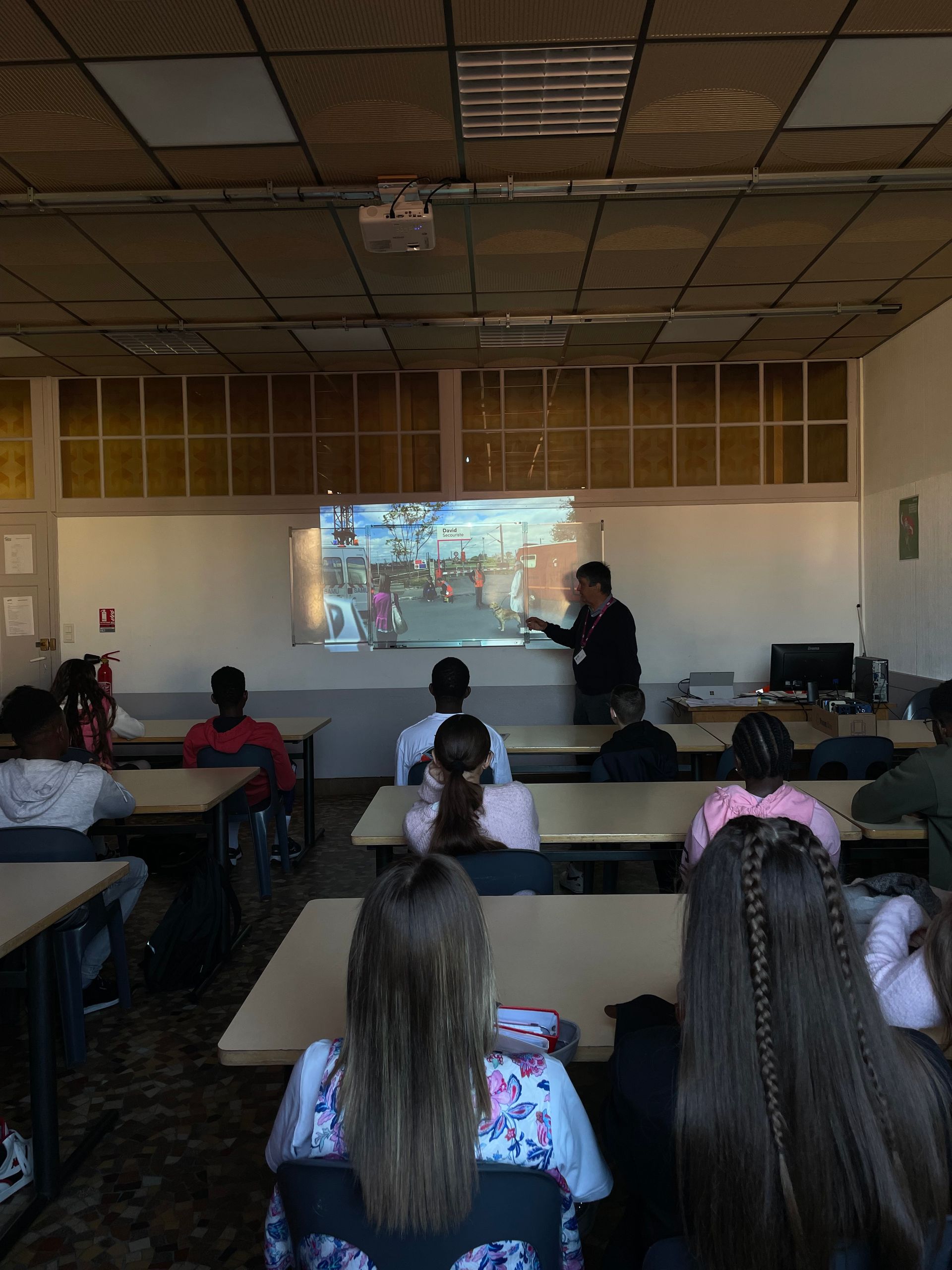Deux élèves regardent une vidéo projetée sur un écran dans une salle de classe.