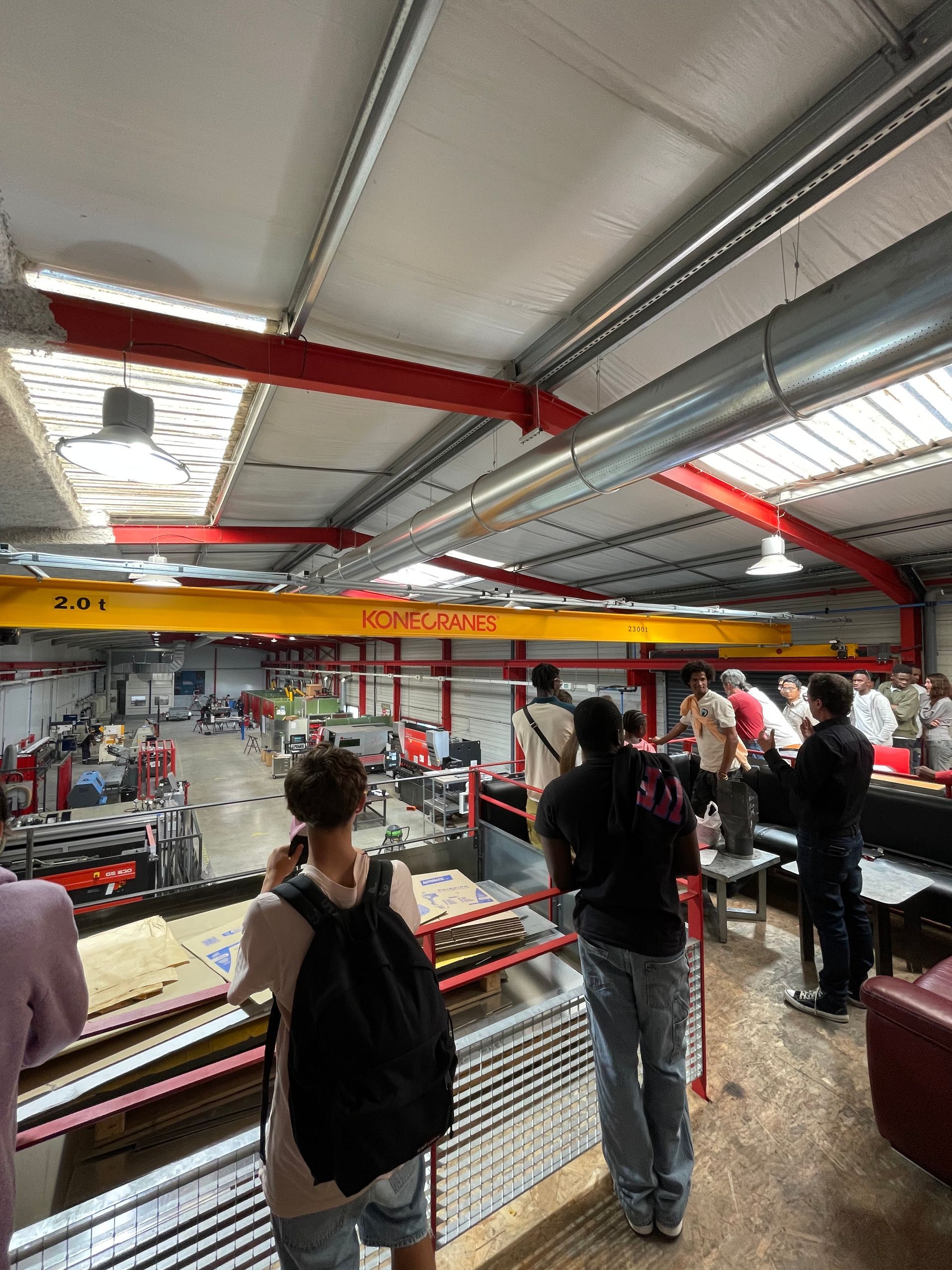 Des élèves dans un atelier de menuiserie observent une démonstration. Beaucoup regardent les établis et le formateur.