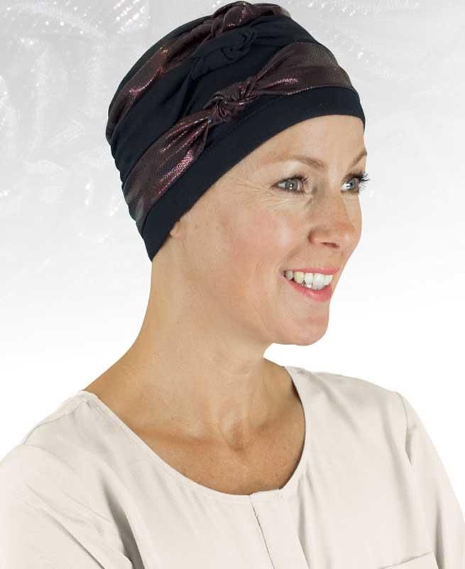 Eine Frau mit schwarzem Turban und weißem Hemd lächelt