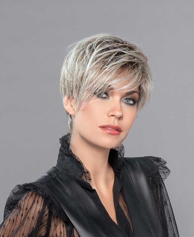 Eine Frau trägt eine kurze blonde Perücke und ein schwarzes Hemd.