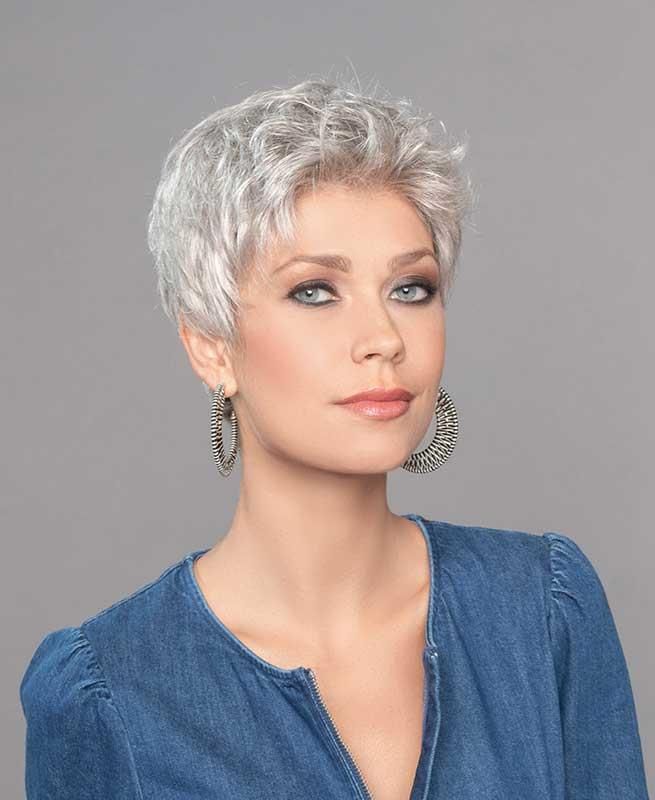 Eine Frau mit grauer Perücke und Ohrringen trägt ein blaues Hemd.