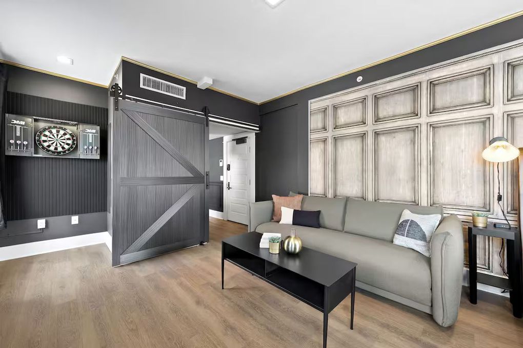Modern living room with gray sofa, black coffee table, wood floor, and large paneled wall decor