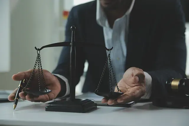 Persona con traje sosteniendo una balanza y un bolígrafo; entorno legal.