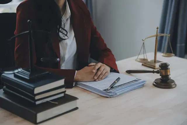 Persona con chaqueta roja en un escritorio con libros de leyes, balanza y mazo.