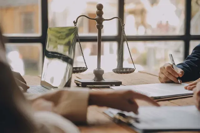 Bufete de abogados: Balanza de la justicia sobre la mesa; la gente revisa documentos.