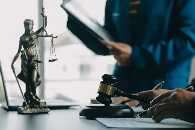 Estatua de la Dama de la Justicia, mazo y documentos legales sobre un escritorio. Abogados revisando documentos.