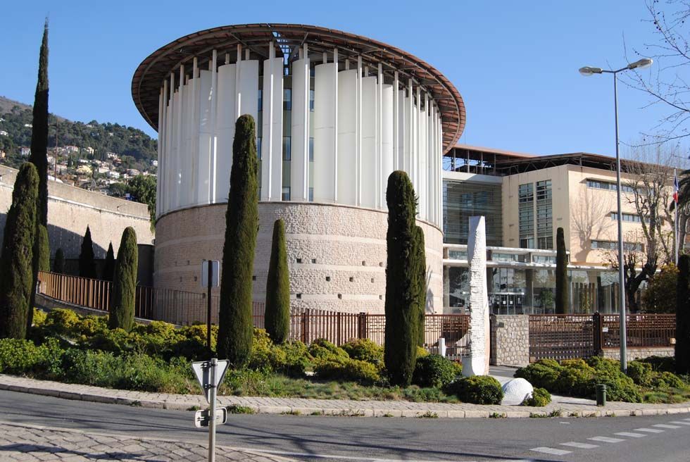 Bâtiment circulaire moderne avec des colonnes blanches, des arbres et des espaces paysagers sous un ciel dégagé