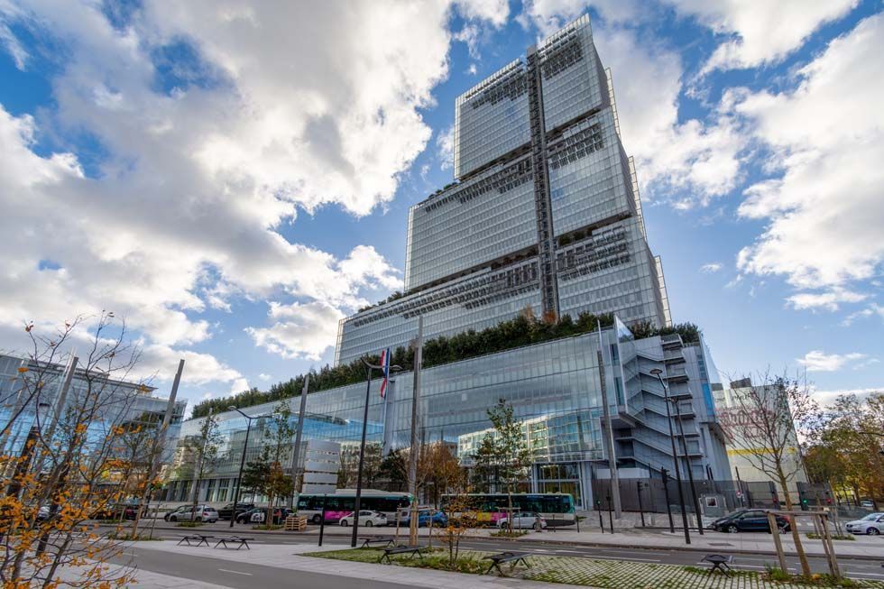 Tour moderne en verre de grande hauteur sous un ciel partiellement nuageux, vue depuis le niveau de la rue