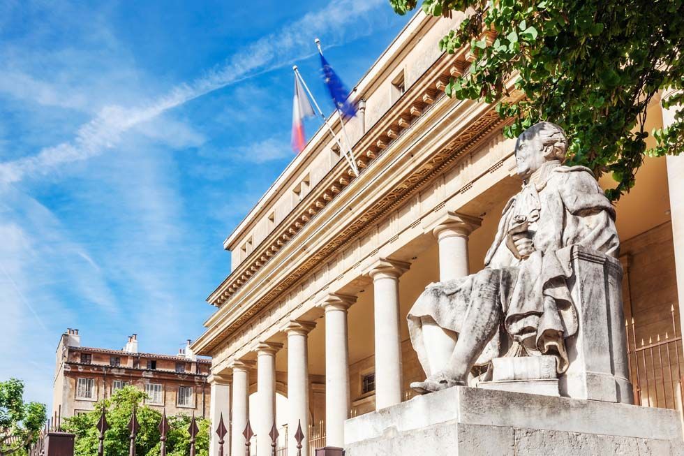 Bâtiment classique avec des colonnes et une statue en pierre sous un ciel bleu, avec des drapeaux au-dessus