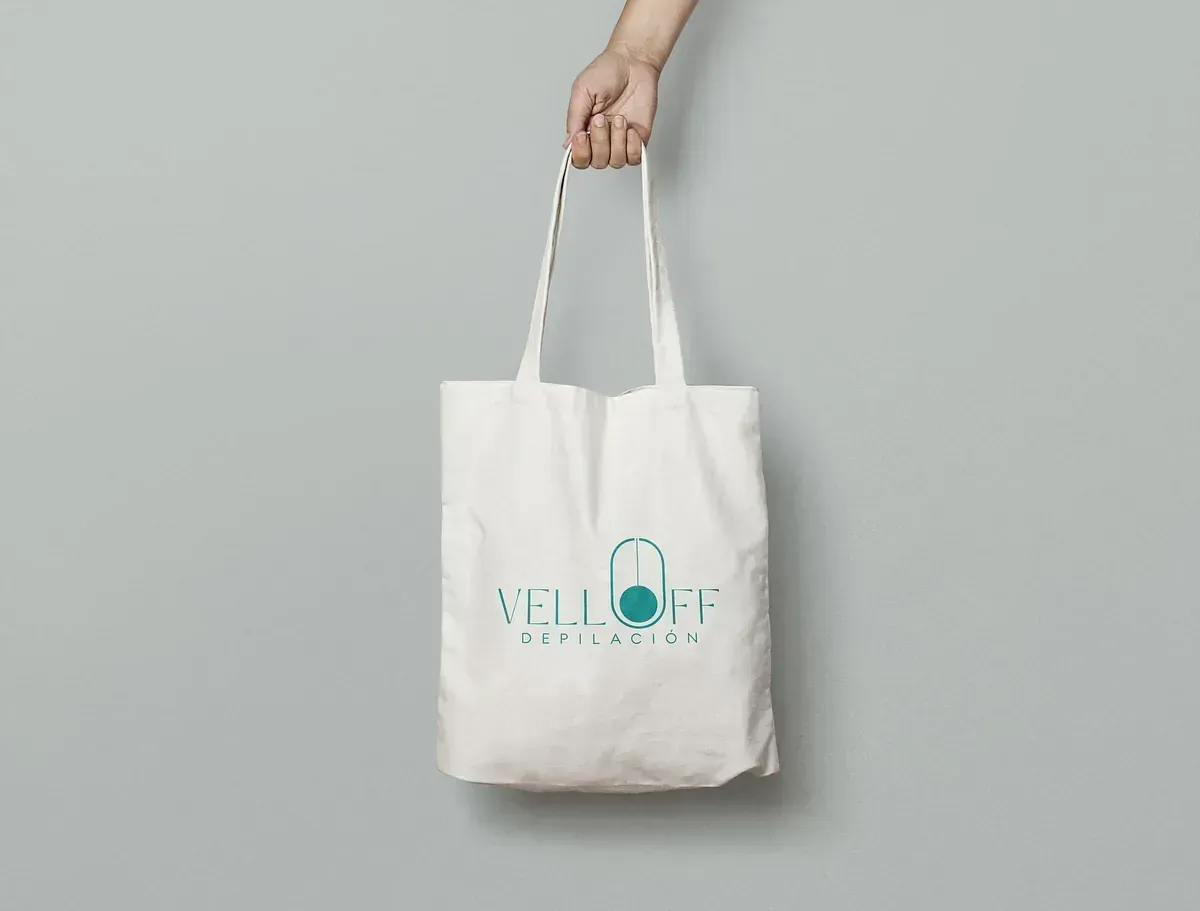 Mano sosteniendo una bolsa de mano blanca con un logotipo verde azulado que dice 