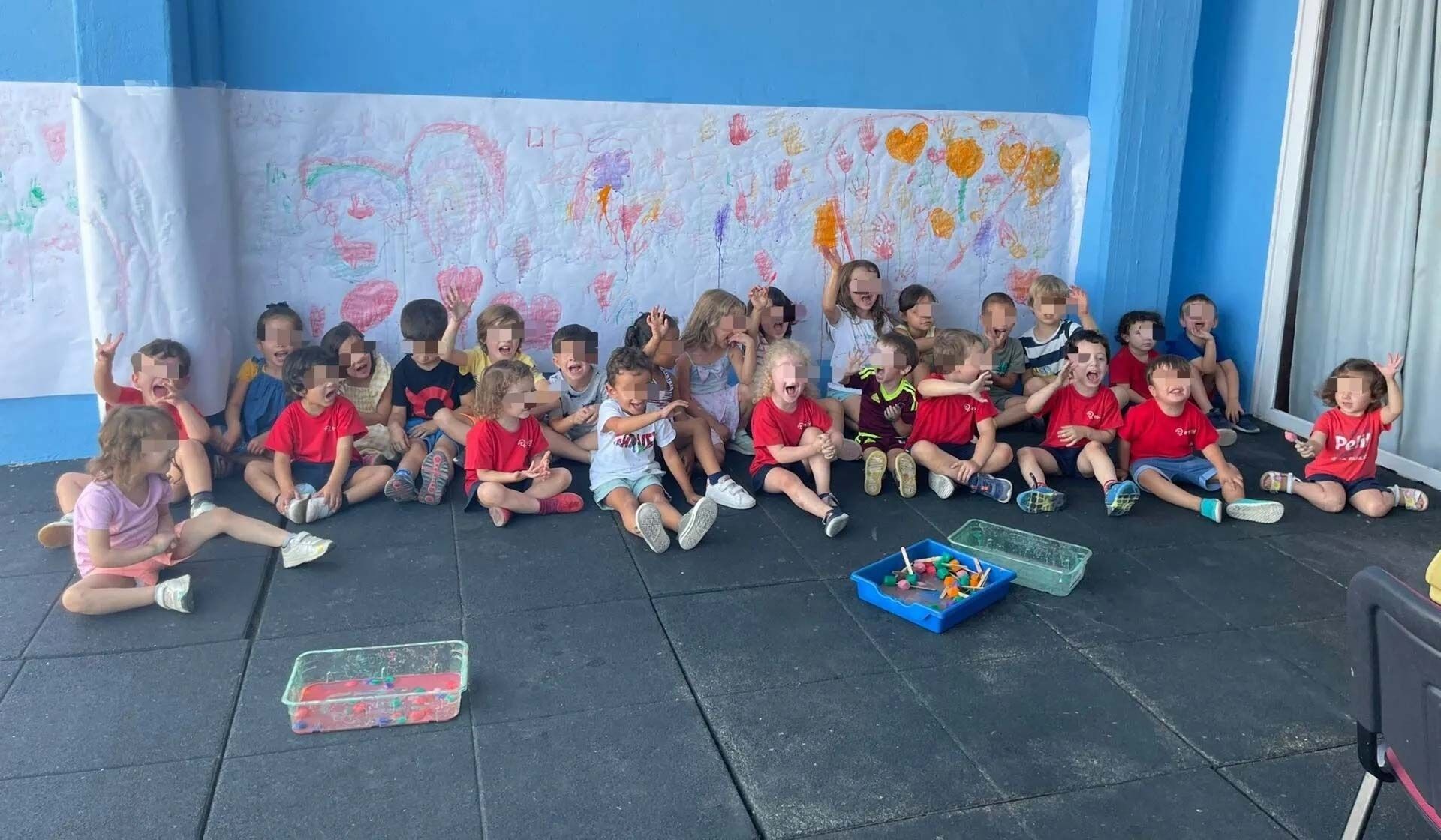Un grupo de niños está sentado en el suelo frente a una pared azul.