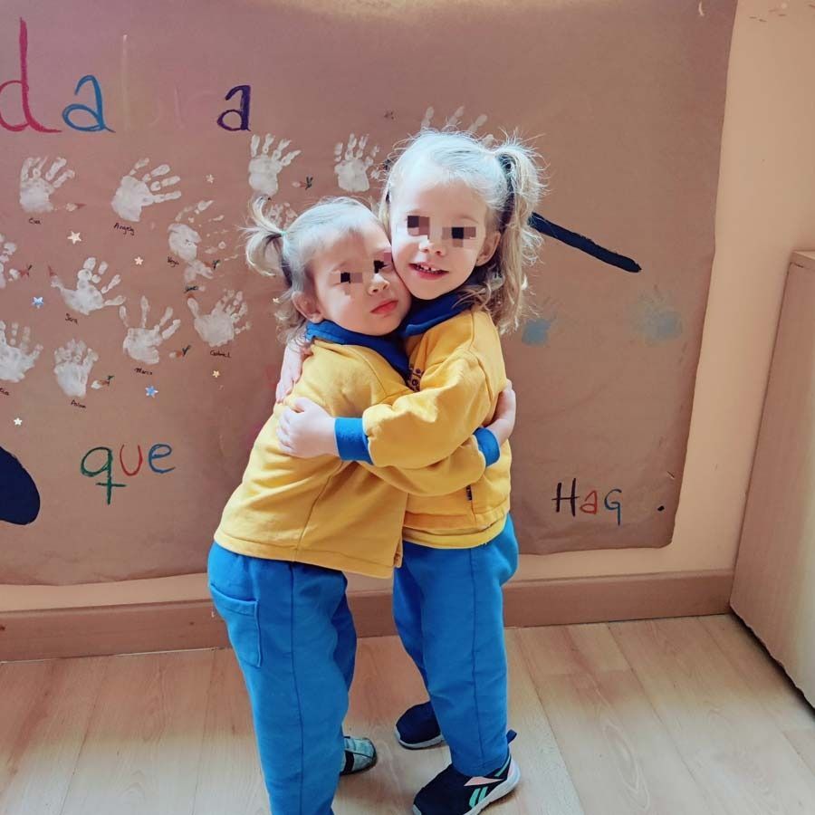 Dos niñas abrazándose frente a un cartel que dice 