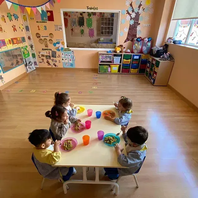 Un grupo de niños están sentados alrededor de una mesa comiendo comida.
