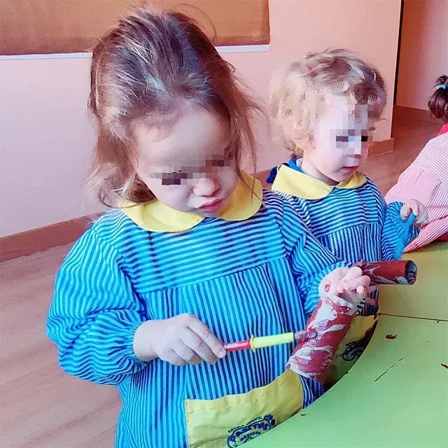 Dos niñas con delantales de rayas azules y amarillas juegan con marcadores.