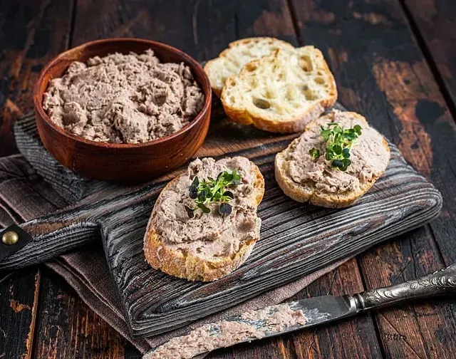 Una tabla de cortar de madera cubierta con rebanadas de pan y un tazón de paté.