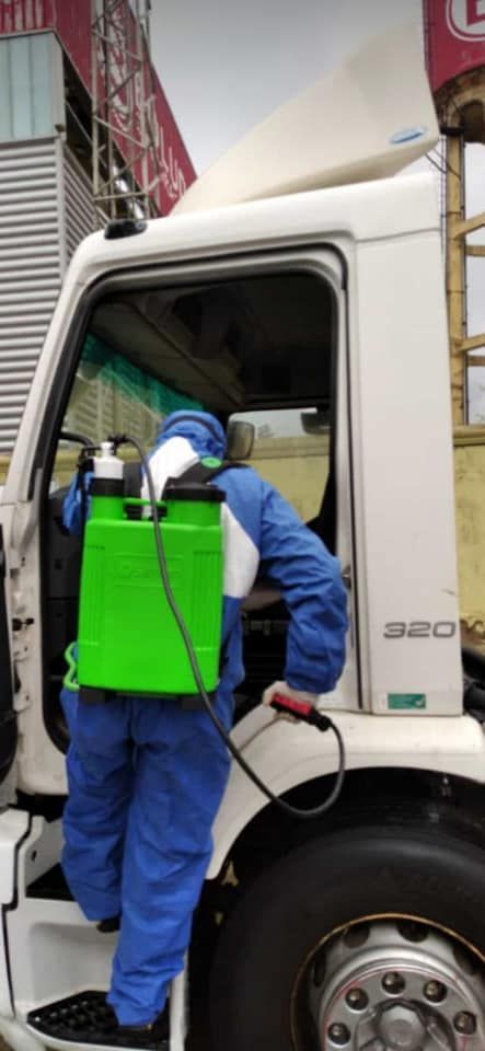 Un hombre con un traje azul está rociando un camión con una mochila verde.