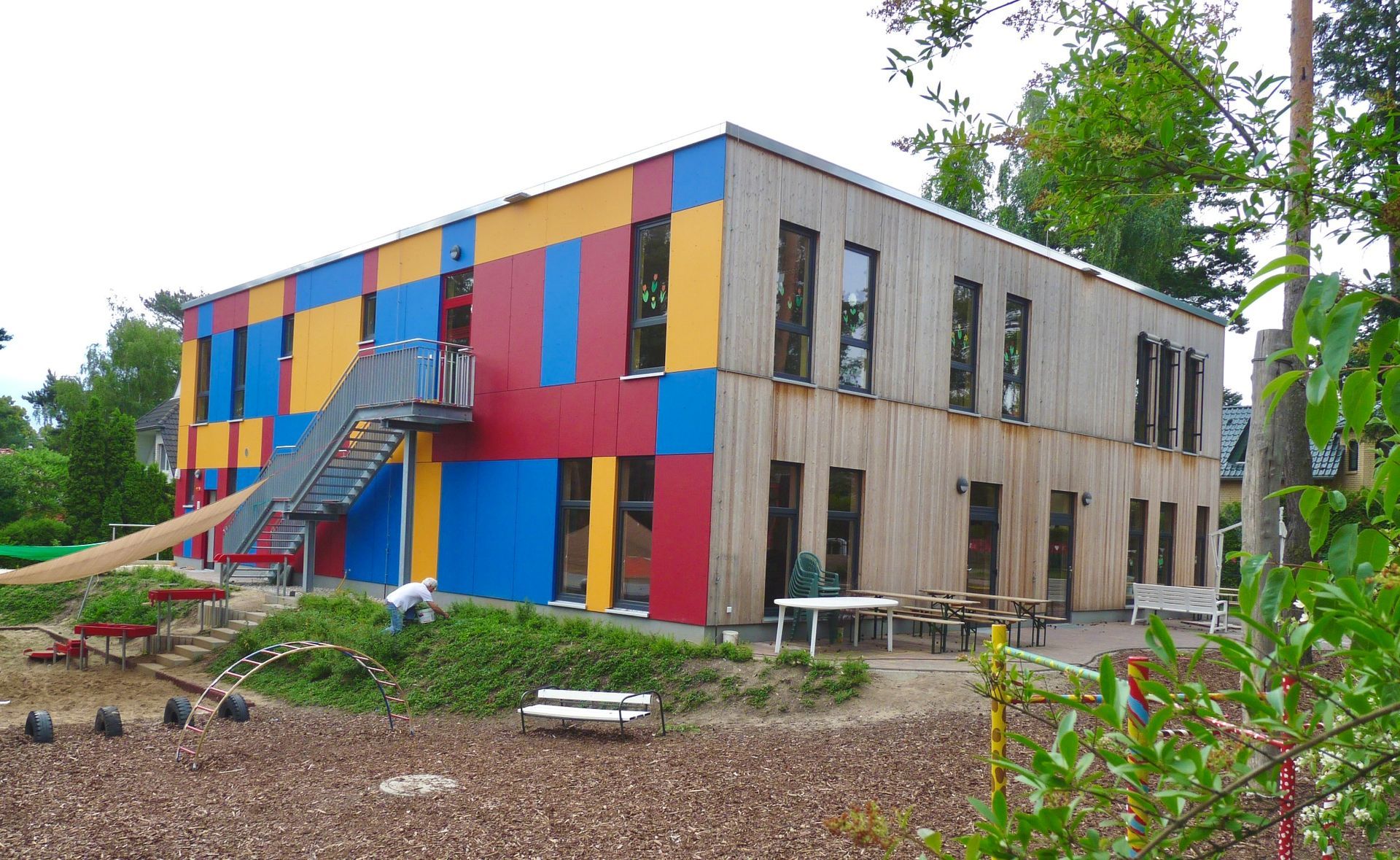 Schulergänzungsbau mit Holzfassade, farbigen Akzentflächen und außenliegender Treppe.