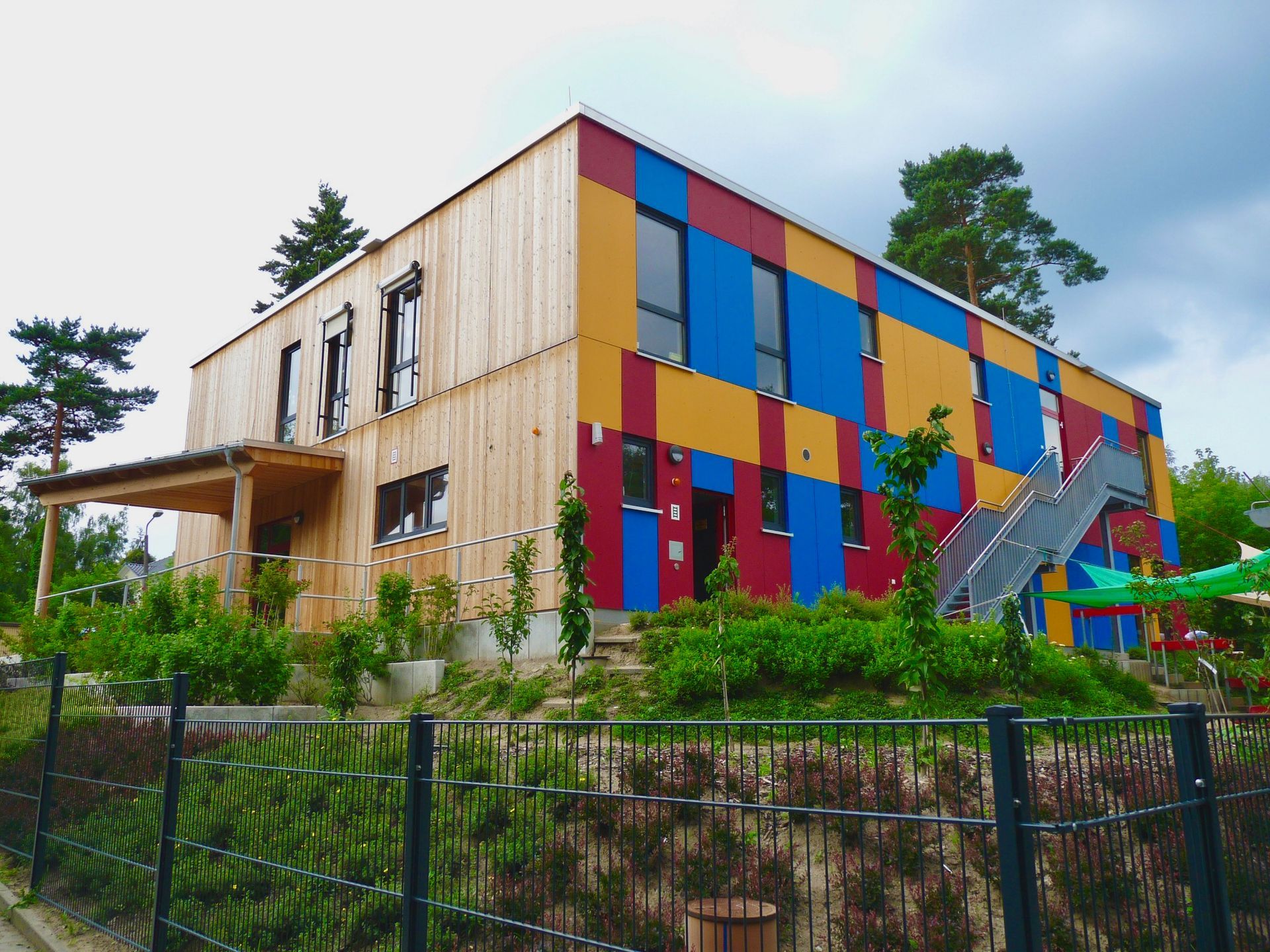 Zweigeschossiger Schulergänzungsbau aus Holz mit farbigen Fassadenelementen und Außentreppe.