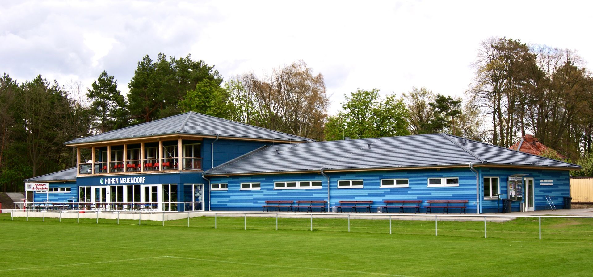 Sportfunktionsgebäude mit blauer Holzfassade auf einem Sportgelände.
