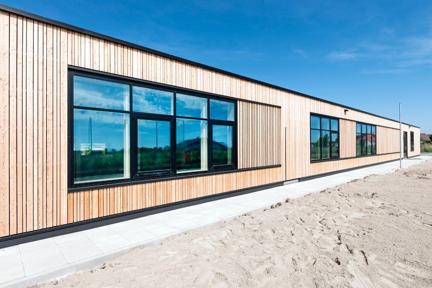 Langgestrecktes Schulgebäude mit Holzverkleidung und großzügigen Fensterflächen.