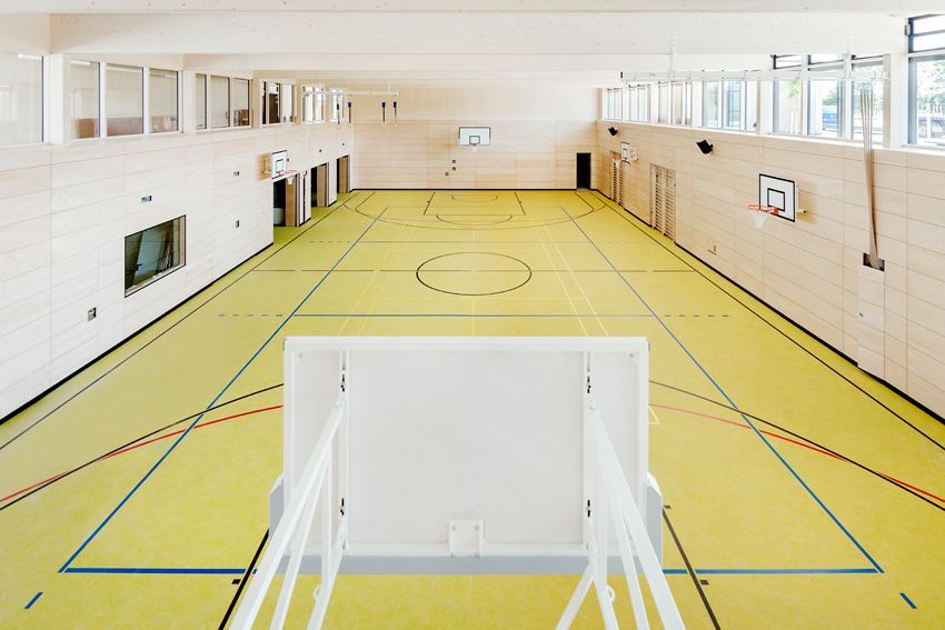 Moderne Schulsporthalle mit Spielfeldmarkierungen, Basketballkörben und Holzinnenwänden.