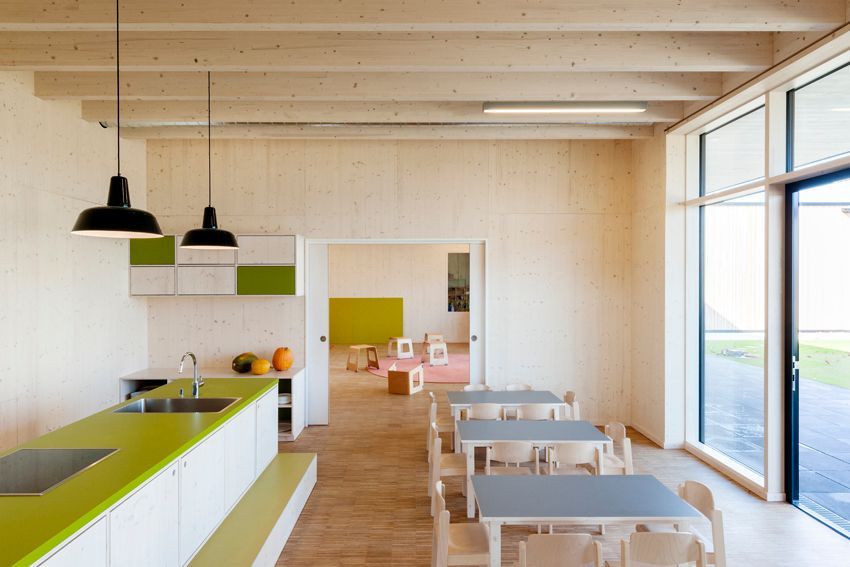 Moderner Unterrichtsraum mit Holzwänden, Küchenzeile und großen Fensterflächen.