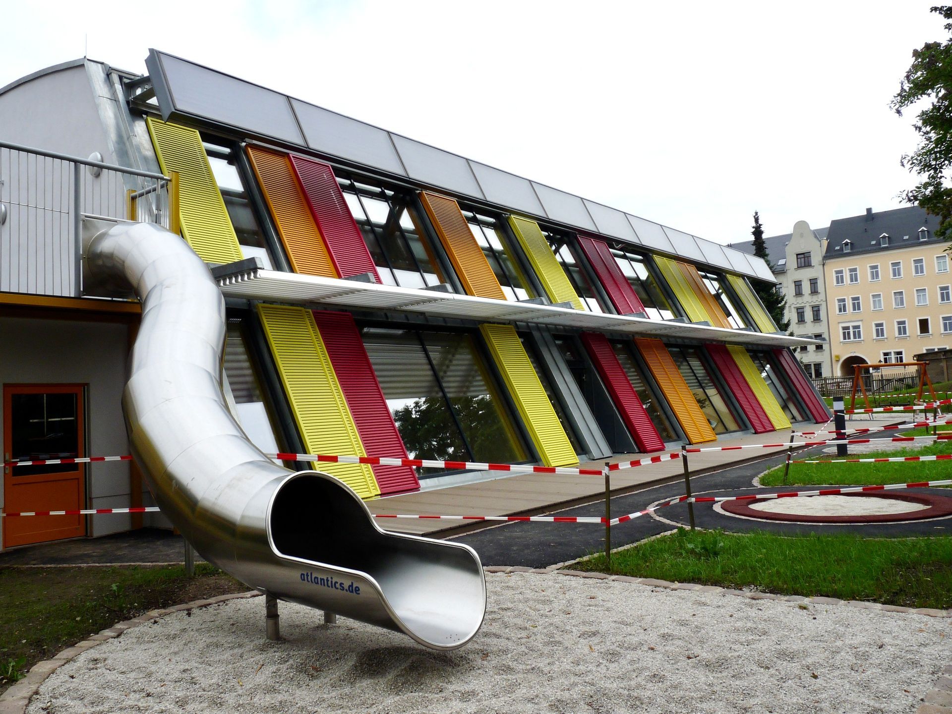 Kindertagesstätte mit außergewöhnlicher Holzarchitektur, farbigen Fassadenelementen und integrierten Rutschen.