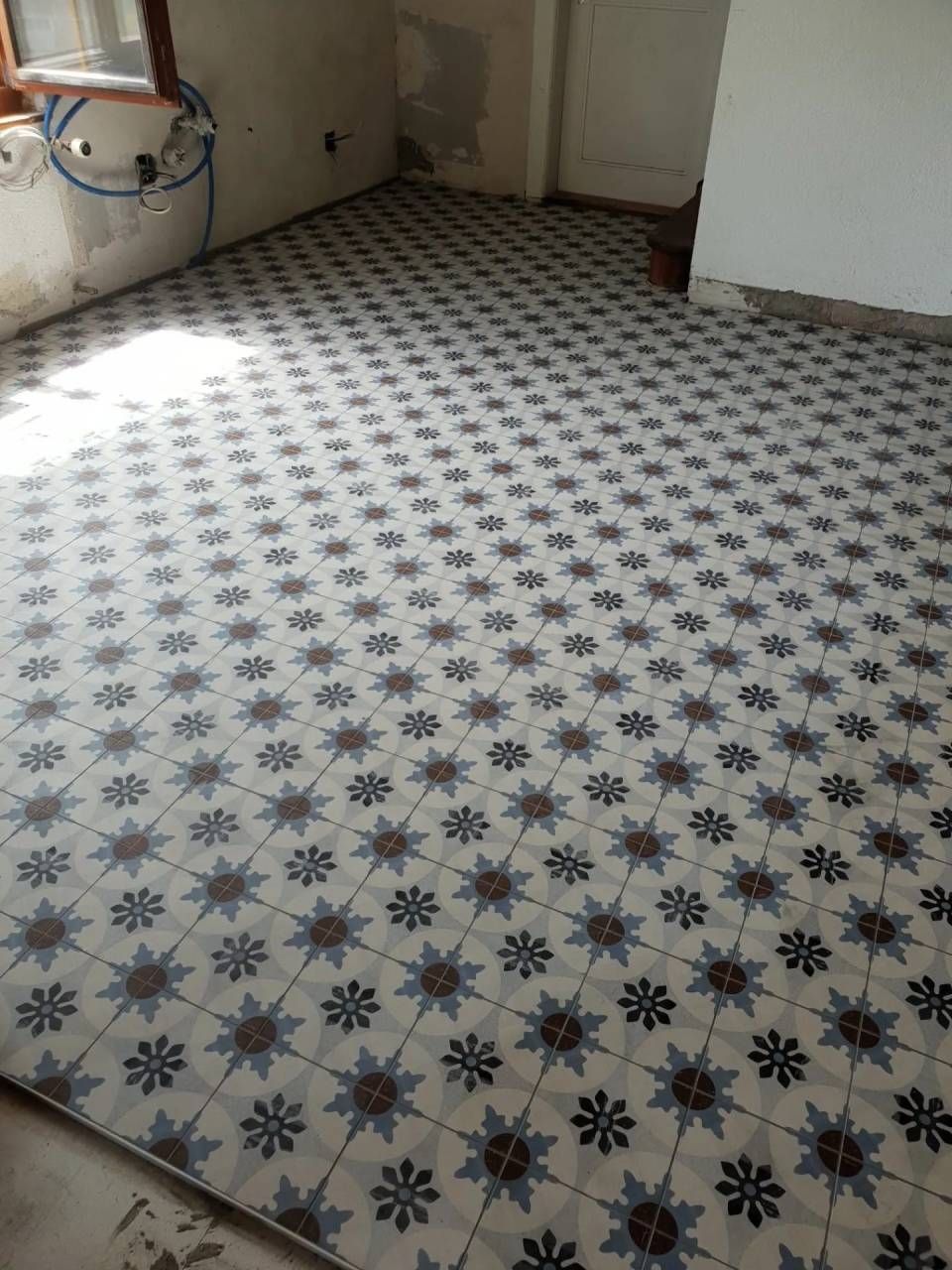 Sol carrelé neuf avec un motif floral bleu et marron répétitif.