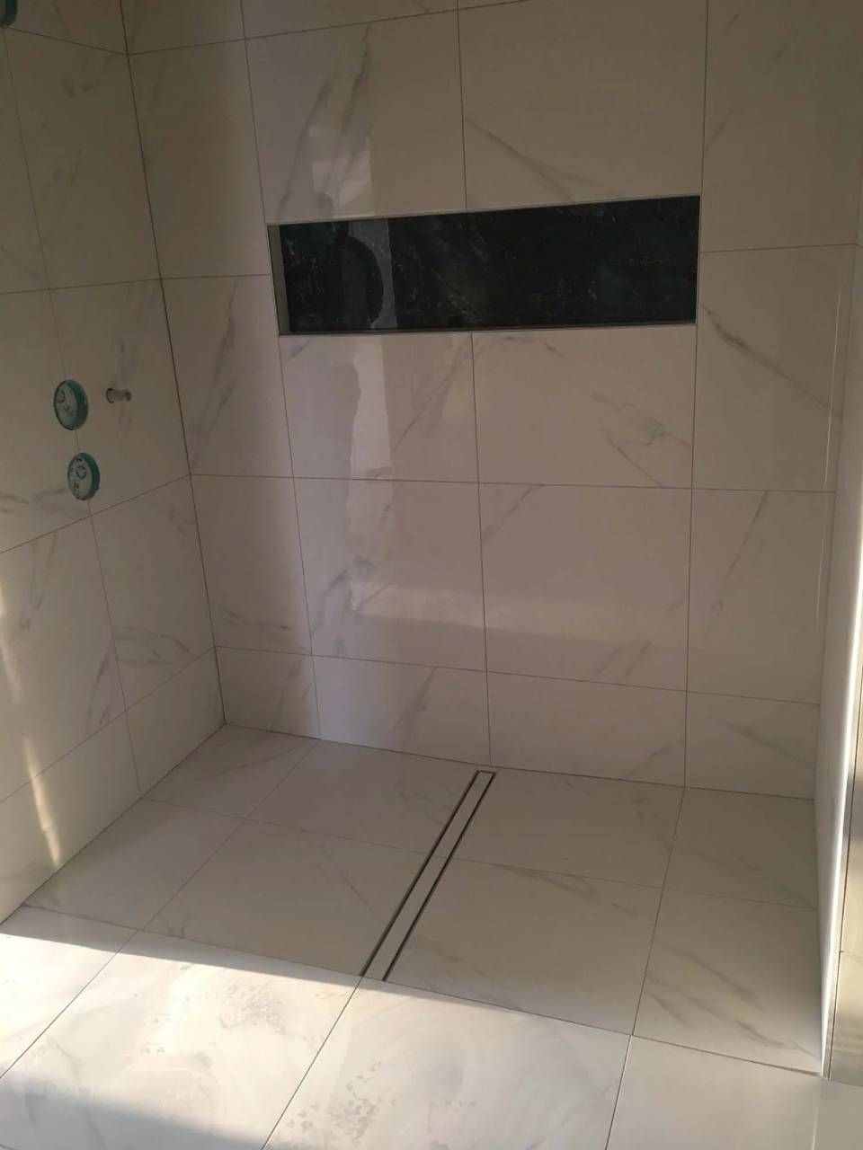 Douche carrelée blanche avec une étagère encastrée noire et un caniveau linéaire.