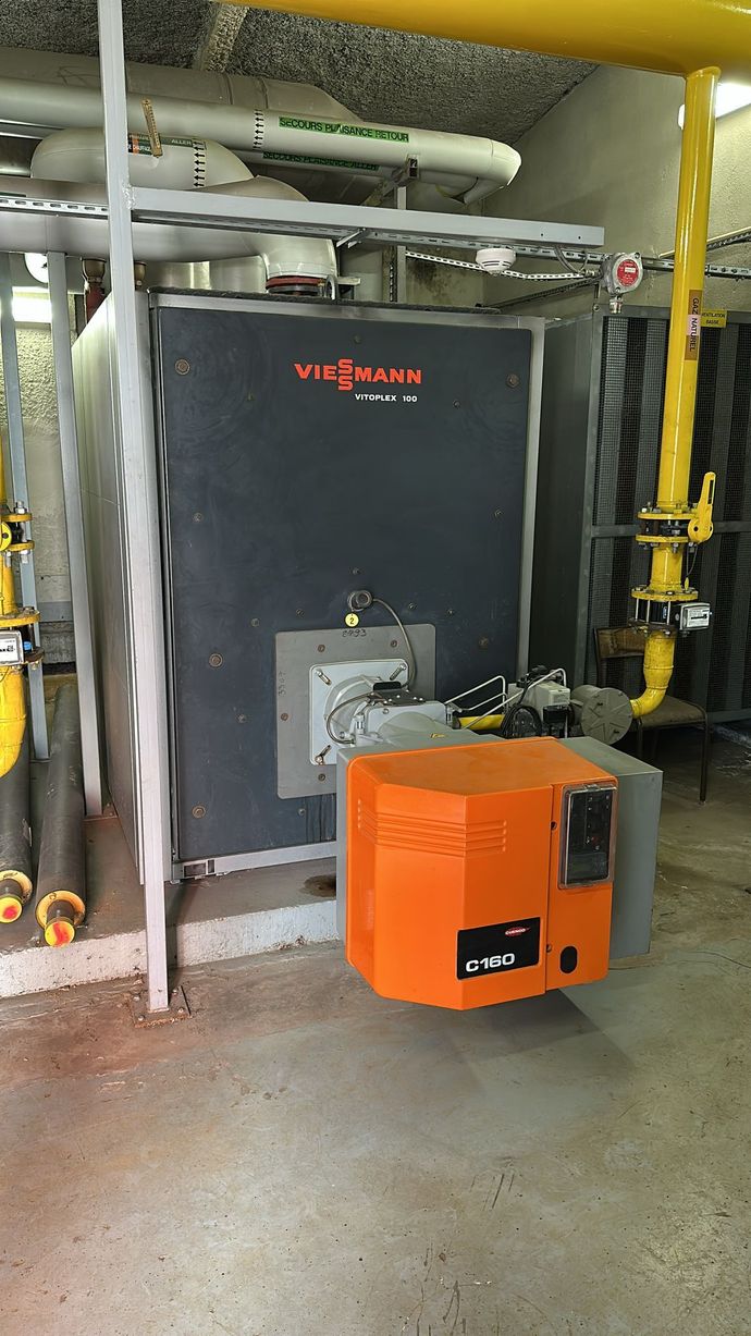 Une grande chaudière orange se trouve dans une pièce avec des tuyaux.