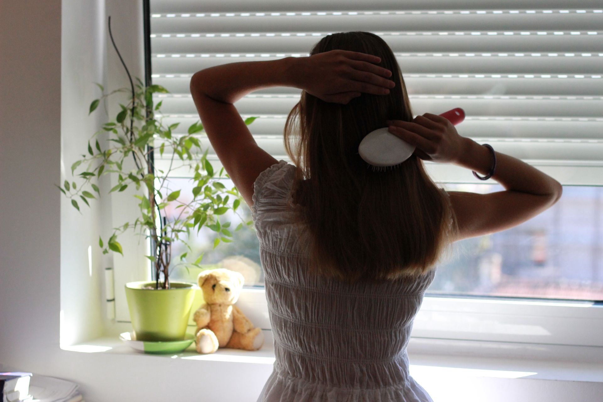 Une femme se coiffe dans sa chambre, les volets à moitié fermés