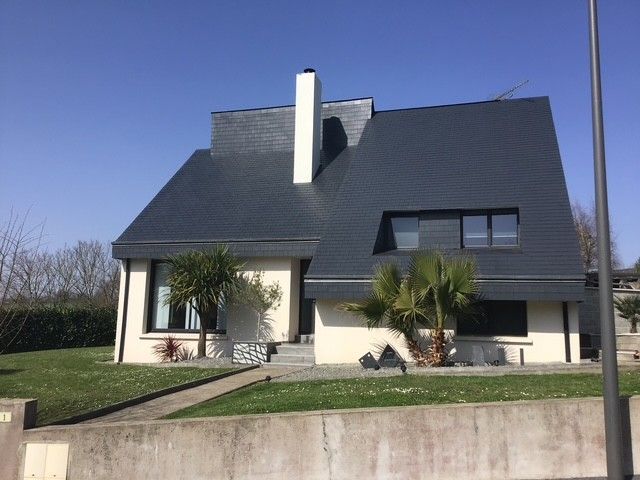Maison en pierre avec toit d'ardoise bleue et tourelle. Portail décoratif en fer forgé et murs en pierre.