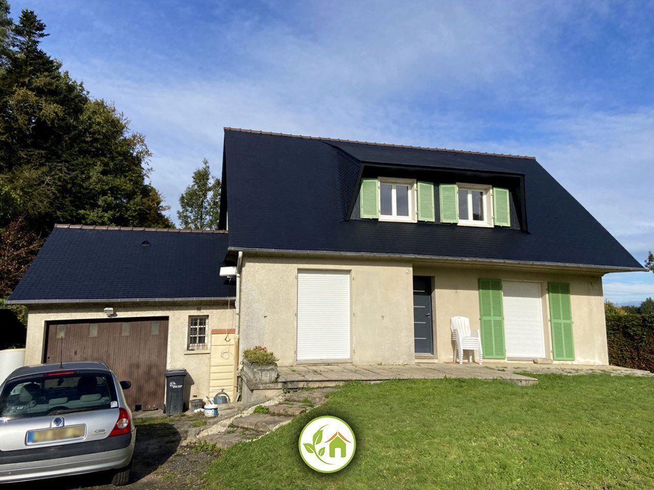 Maison beige avec toit noir, volets verts, garage et voiture garée devant.