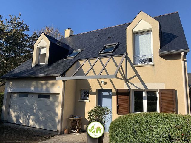 Maison beige à deux étages avec un toit en ardoise, des lucarnes et un petit auvent au-dessus de la porte d'entrée.