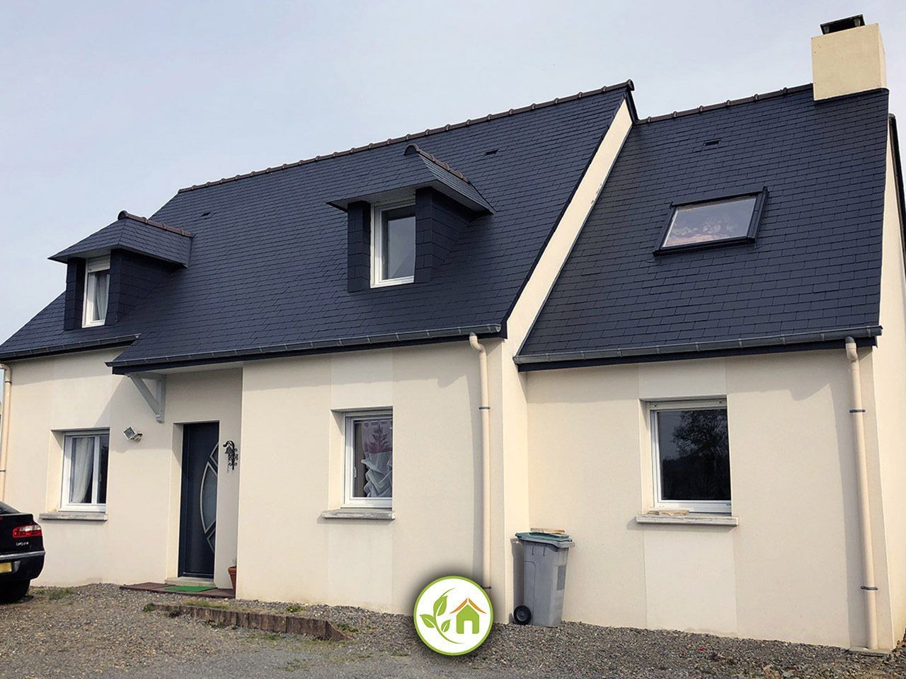 Maison beige avec un toit en ardoise bleu foncé et trois petites lucarnes.