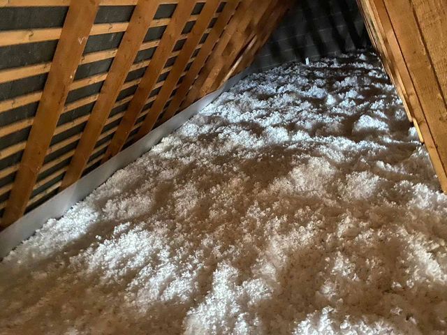 Combles remplis d'une épaisse couche d'isolant blanc entre des chevrons en bois.