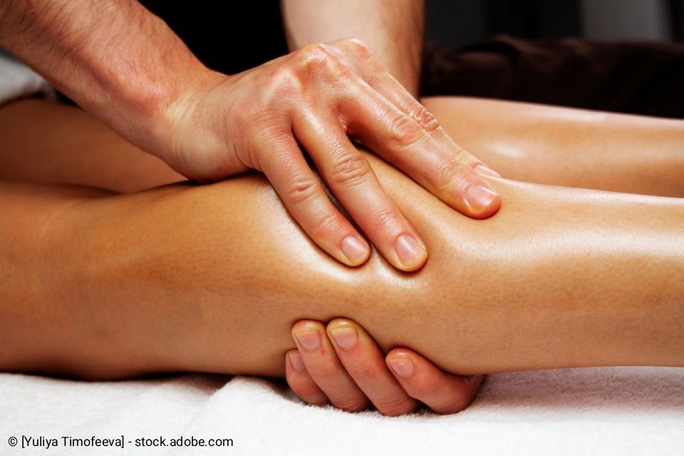 Hände massieren den Unterschenkel einer Person, die auf einer weißen Fläche liegt.