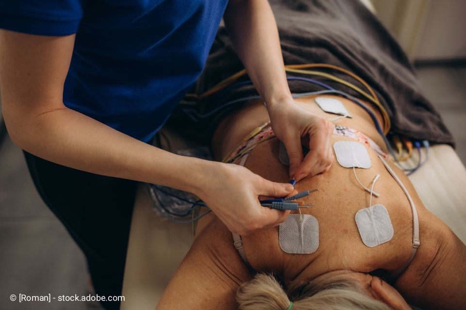 Therapeut befestigt Elektroden am Rücken des Patienten zur Behandlung;