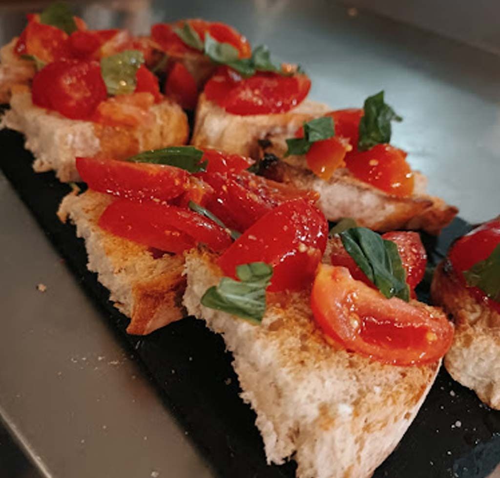Una rebanada de pan con tomates y albahaca encima.