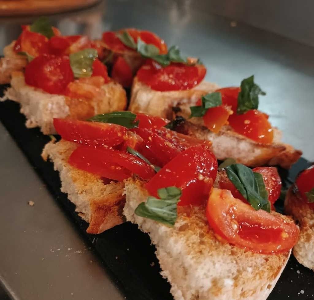 Una hilera de rebanadas de pan cubiertas con tomates y albahaca.