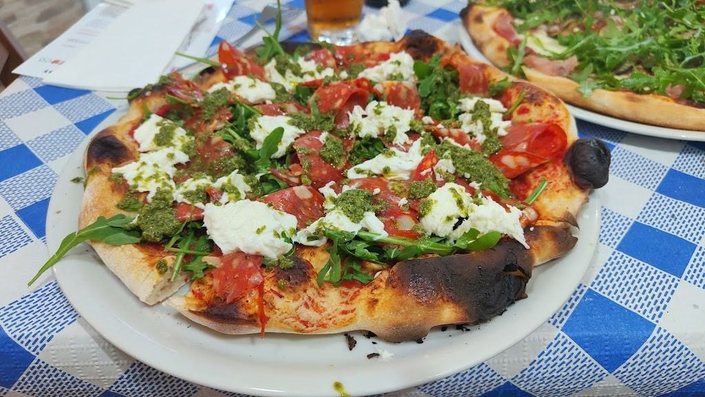 Una pizza con tomates y queso está en un plato blanco sobre una mesa.