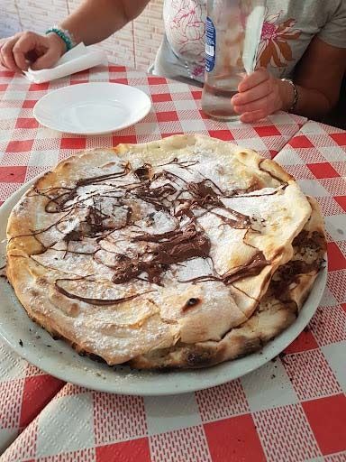 Una pizza con chocolate y azúcar en polvo encima está en un plato sobre un mantel a cuadros.