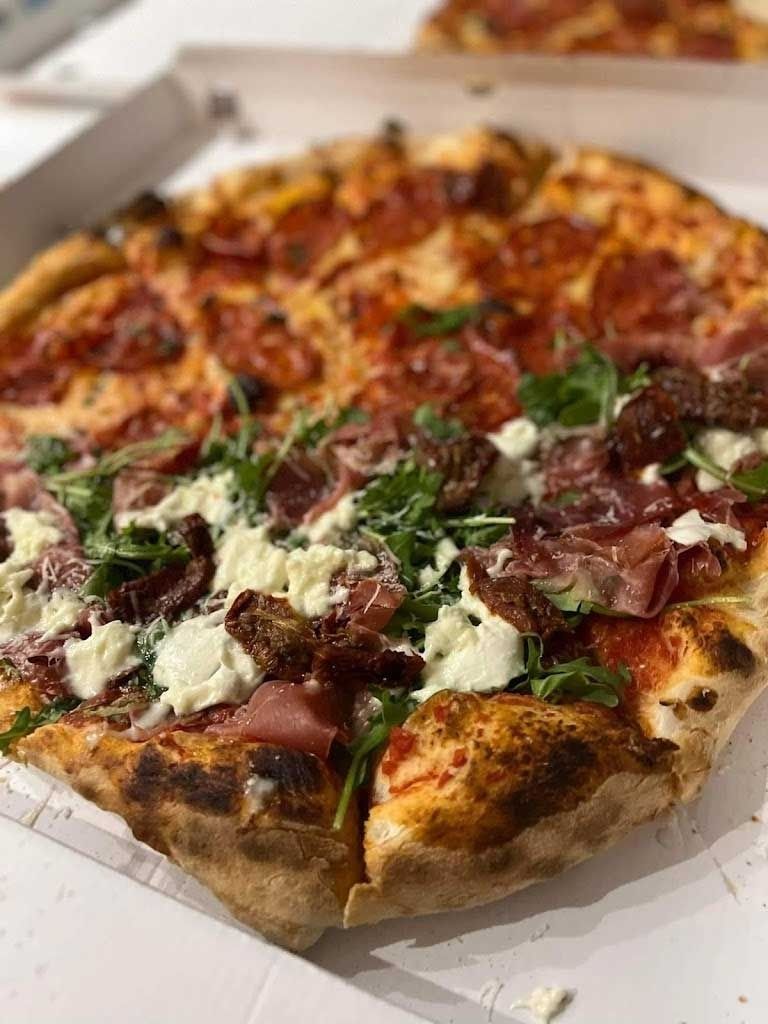 Una pizza con muchos ingredientes está en una caja sobre una mesa.