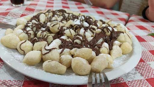 Un plato blanco cubierto con ñoquis y salsa de chocolate sobre un mantel a cuadros.