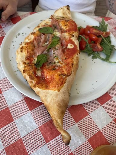Un plato blanco cubierto con una rebanada de pizza y tomates sobre un mantel a cuadros.