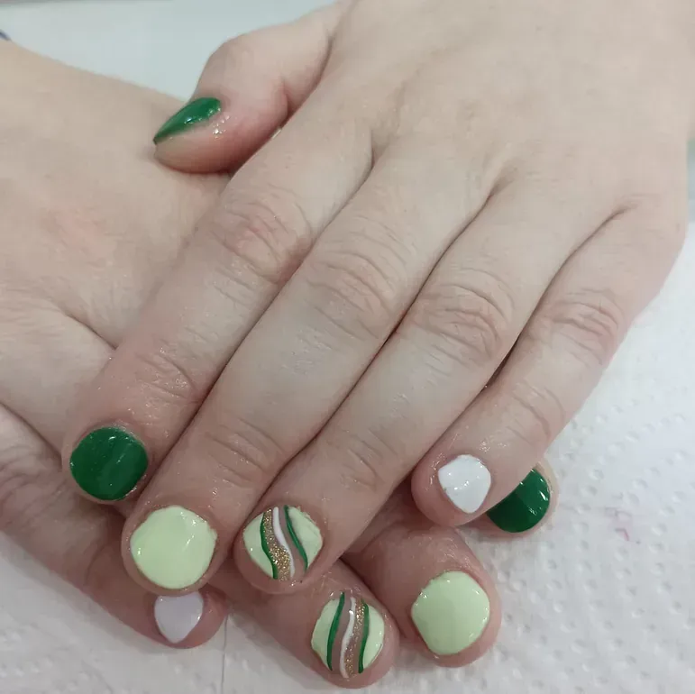 Un primer plano de las manos de una persona con uñas verdes y blancas.
