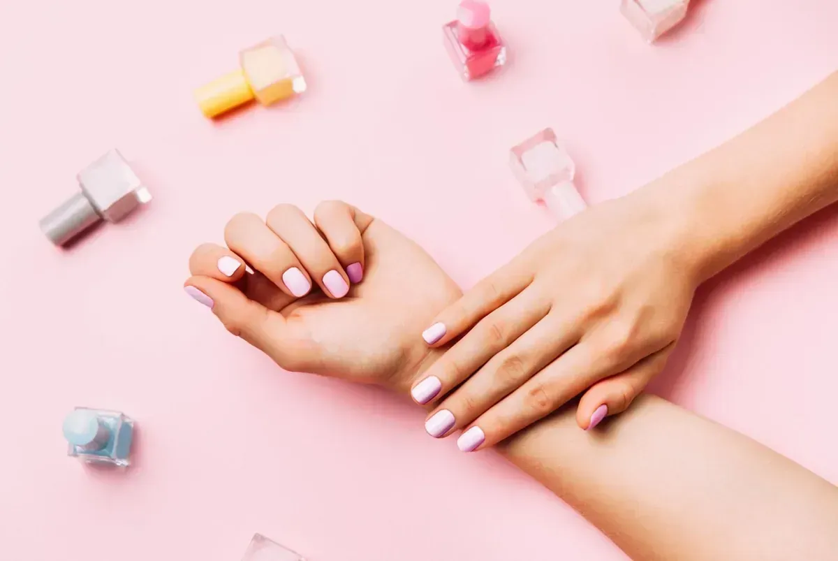 Manos de mujer con esmalte de uñas rosa sobre un fondo rosa.